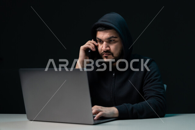 Spying on phone calls, exposure to electronic attacks and hacking, hacking systems and protecting devices, stealing passwords and confidential data, close-up portrait of a young Arab Gulf Emirati man wearing a black jacket working in the field of illegal hacking, black background