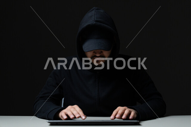 سرقة كلمات المرور والبيانات السرية، اختراق الأنظمة وحماية الأجهزة, التعرض للهجمات والاختراقات الالكترونية, مفهوم الجرائم الالكترونية, بورتريه مقرب لشاب عربي خليجي إماراتي يرتدي سترة سوداء يعمل في مجال الهكر الغير قانوني, خلفية سوداء