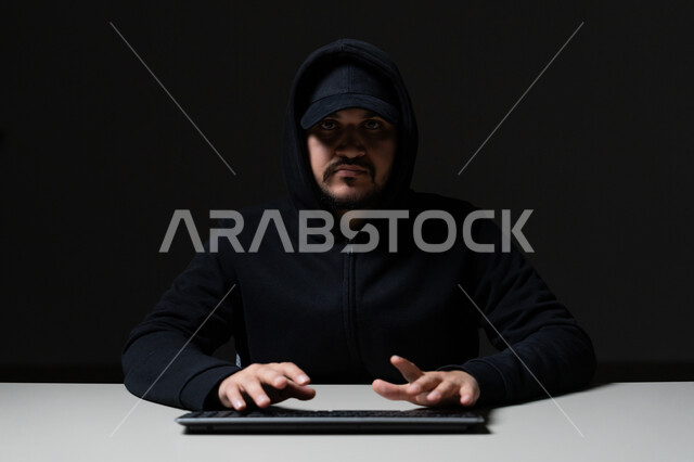 خوارزميات لتدمير الحسابات الرقمية, استخدم جهاز الحاسوب لأغراض غير قانونية, التسلل عبر الأمن السيبراني، قرصنة وسرقة البيانات, بورتريه مقرب لشاب عربي خليجي إماراتي يرتدي سترة سوداء يعمل في مجال الهكر, خلفية سوداء
