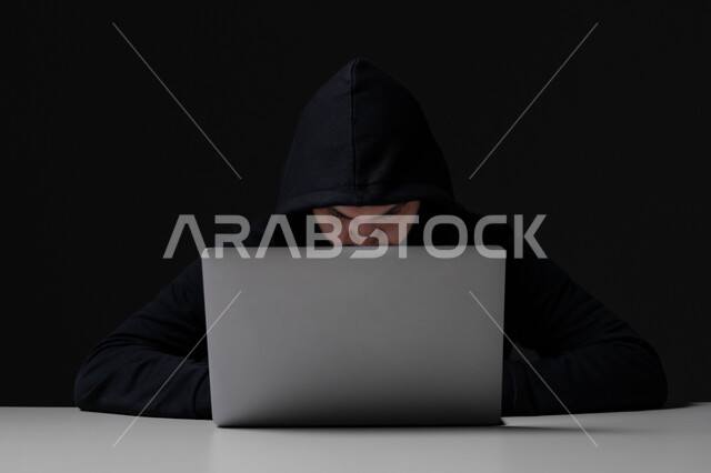 Use computer for illegal purposes, cyber security intrusion, data hacking and theft, close-up portrait of young Emirati Gulf Arab man wearing black jacket working in hacking field, black background