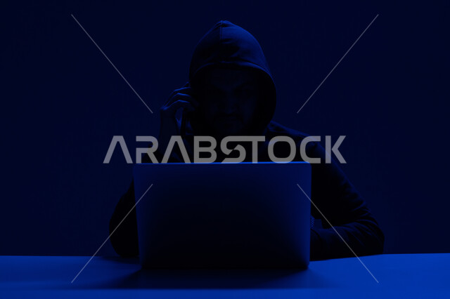 خوارزميات لتدمير الحسابات الرقمية, استخدم جهاز الحاسوب لأغراض غير قانونية, التسلل عبر الأمن السيبراني، قرصنة وسرقة البيانات, بورتريه مقرب لشاب عربي خليجي إماراتي يرتدي سترة سوداء يعمل في مجال الهكر, خلفية زرقاء