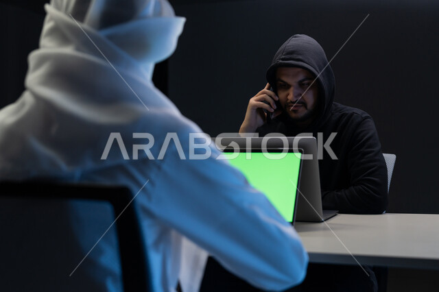اختراق حماية وأمن وخصوصية المستخدمين، مفهوم الجرائم الالكترونية, التعرض للهجمات والاختراقات, بورتريه مقرب من الخلف لرجل عربي خليجي إماراتي يرتدي الكندورة والغترة البيضاء يعمل على جهاز الحاسوب, عرض شاشة خضراء عبر الحاسوب, كروما, خلفية سوداء