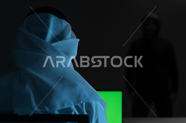 اختراق حماية وأمن وخصوصية المستخدمين، مفهوم الجرائم الالكترونية, التعرض للهجمات والاختراقات, بورتريه مقرب من الخلف لرجل عربي خليجي إماراتي يرتدي الكندورة والغترة البيضاء يعمل على جهاز الحاسوب, عرض شاشة خضراء عبر الحاسوب, كروما, خلفية سوداء