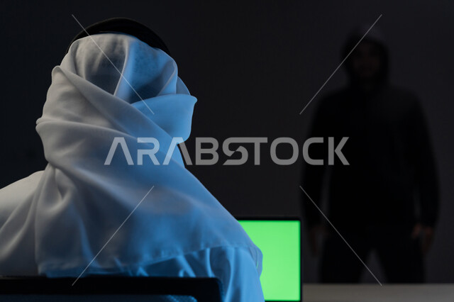 التعرض للهجمات والاختراقات، اختراق حماية وأمن وخصوصية المستخدمين، مفهوم الجرائم الالكترونية, بورتريه مقرب من الخلف لرجل عربي خليجي إماراتي يرتدي الكندورة والغترة البيضاء يعمل على جهاز الحاسوب, عرض شاشة خضراء عبر الحاسوب, كروما, خلفية سوداء