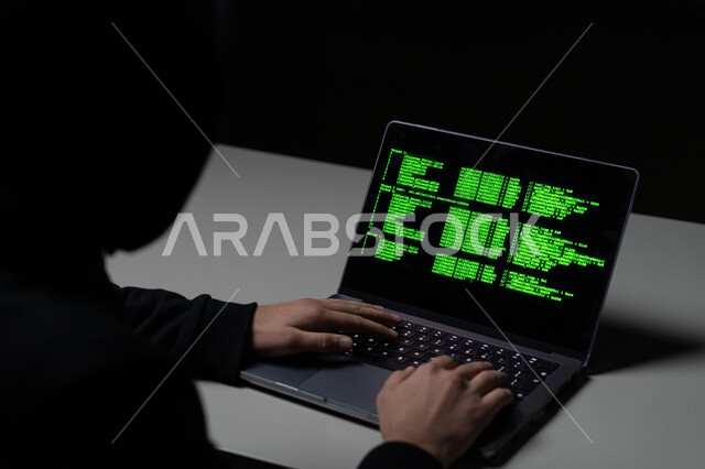 تطوير وبناء المواقع والتطبيقات, استخدام لغات البرمجة، القدرة على اختراق حماية الأجهزة ،أكواد وخوارزميات برمجية, مفهوم الجرائم الالكترونية, بورتريه مقرب من الخلف لشاب عربي خليجي إماراتي يرتدي سترة سوداء يعمل في مجال الهكر الغير قانوني, خلفية سوداء