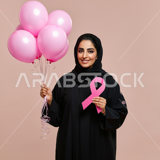 اليوم العالمي للكشف المبكر عن سرطان الثدي, الحملات التوعوية ضد الأمراض الخبيثة, بورتريه مقرب لإمرأة عربية خليجية سعودية مبتسمة محجبة ترتدي العباءة تمسك بيدها الشريط الوردي ومجموعة من البلالين وتنظر إلى الكاميرا بقوة, خلفية وردية