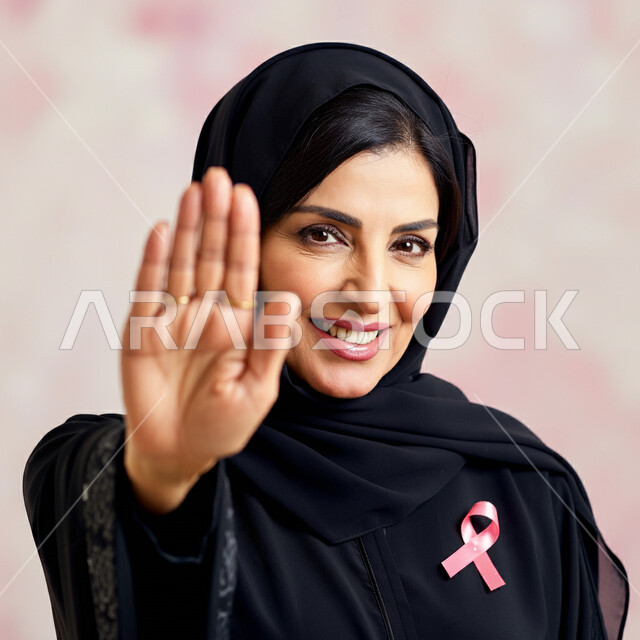 Breast cancer awareness campaign, prevention and stopping neglect of early detection, close-up portrait of a Saudi Arabian Gulf woman wearing hijab and abaya, putting on a pink ribbon, raising her hand with gestures of rejection and strength, challenging diseases and malignant tumors, symbol of the global campaign, pink background