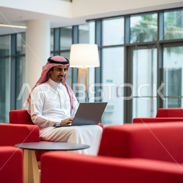 استخدام الاجهزة التقنية الحديثة، رجل عربي خليجي سعودي يرتدي الشماغ والثوب التقليدي يجلس في قاعة انتظار الفندق يستخدم الحاسوب المحمول، إدارة مهام العمل اليومية وعقد الاجتماعات عن بعد، المهن والوظائف السعودية، تصفح مواقع التواصل الاجتماعي 