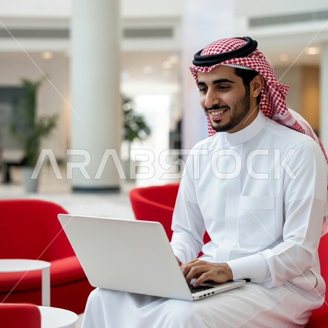 إدارة مهام العمل اليومية وعقد الاجتماعات عن بعد، استخدام الاجهزة التقنية الحديثة، رجل عربي خليجي سعودي يرتدي الشماغ والثوب التقليدي يجلس في قاعة انتظار الفندق يستخدم الحاسوب المحمول، المهن والوظائف السعودية، تصفح مواقع التواصل الاجتماعي 