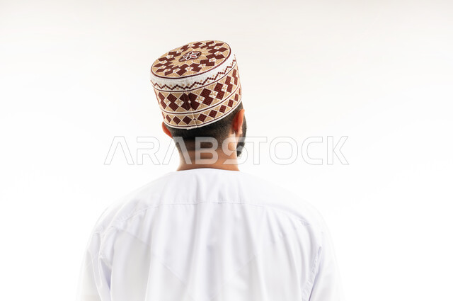 النظر الى شيء ما، الاناقة والمظهر الخارجي، بورتريه مقرب من الخلف لرجل عربي خليجي عماني يرتدي الدشداشة والكمه العمانية، خلفية بيضاء
