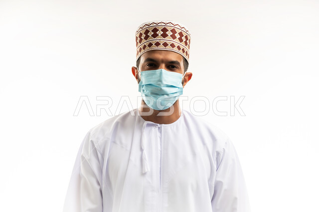 الاهتمام بالاناقة والمظهر الخارجي، اتباع الإجراءات الاحترازية لمنع انتشار العدوى، بورتريه مقرب لشاب عربي خليجي عماني يرتدي الدشداشة والكمه يضع الكمامة الطبية لتجنب الاصابة بالامراض، اتخاذ التدابير اللازمة للوقاية من فيروس كورونا، خلفية بيضاء