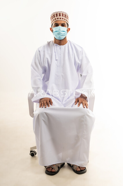 الاهتمام بالاناقة والمظهر الخارجي، اتباع الإجراءات الاحترازية لمنع انتشار العدوى، بورتريه لشاب عربي خليجي عماني يرتدي الدشداشة والكمه يضع الكمامة الطبية لتجنب الاصابة بالامراض، اتخاذ التدابير اللازمة للوقاية من فيروس كورونا، خلفية بيضاء