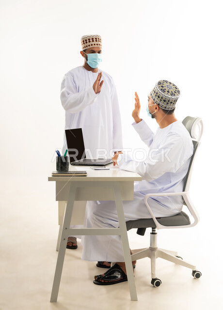 اتباع الاجراءات الوقائية لفايروس كورونا, ، دمج التقنيات الحديثة في الحياة العملية, بورتريه من الجانب لشابان عربيان خليجيان عمانيان يرتديان الدشداشة والكمه والكمامة الطبية يقومان بالقاء التحية والحفاظ على المسافات، خلفية بيضاء