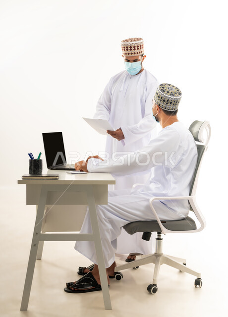 اتخاذ الاجراءات الوقائية لفايروس كورونا, ارتداء الكمامة الطبية للحفاظ على الصحة, بورتريه من الجانب لرجل عربي خليجي عماني يرتدي الدشداشة والكمه يقوم بإعطاء التعليمات وشرح المهام لزميله، الرقي واللطف في التعامل بين الموظفين، مفهوم المشاركة في العمل، خلفية بيضاء