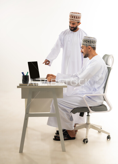 مفهوم المشاركة في العمل، تبادل الخبرات و المهارات بين الموظفين, دمج التقنيات الحديثة في الحياة العملية، بورتريه من الجانب لرجل عربي خليجي عماني يرتدي الدشداشة والكمه يشير باصبع السبابة الى الحاسب المحمول، خلفية بيضاء