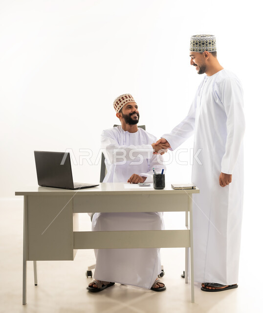 حسن الاستقبال بين زملاء العمل, اللطف والرقي في التعامل، بورتريه لشابان عربيان خليجيان عمانيان يرتديان الدشداشة والكمه يقومان بمصافحة اليدين بايماءات السرور، خلفية بيضاء