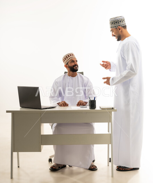 نقاشات وحوارات عمل بين الموظفين، دمج التقنيات الحديثة في الحياة العملية, بورتريه لشابان عربيان خليجيان عمانيان يرتديان الدشداشة والكمه يقومان بتبادل الاحاديث بايماءات السعادة، خلفية بيضاء