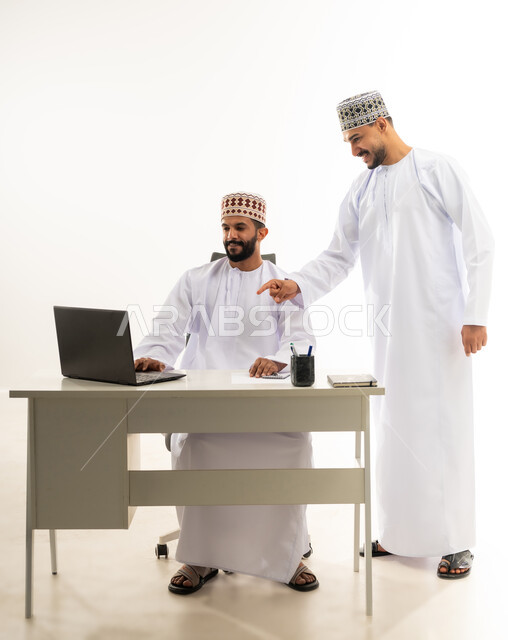 مفهوم المشاركة في العمل، تبادل الخبرات و المهارات بين الموظفين, دمج التقنيات الحديثة في الحياة العملية، بورتريه لرجل عربي خليجي عماني يرتدي الدشداشة والكمه يشير باصبع السبابة الى الحاسب المحمول، خلفية بيضاء