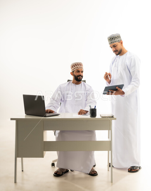 استخدام الاجهزة والتقنيات الحديثة, بورتريه لرجل عربي خليجي عماني يرتدي الدشداشة والكمه يقوم بإعطاء التعليمات وشرح المهام لزميله، الرقي واللطف في التعامل بين الموظفين، مفهوم المشاركة في العمل، خلفية بيضاء