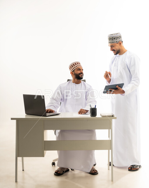 استخدام الاجهزة والتقنيات الحديثة, بورتريه لرجل عربي خليجي عماني يرتدي الدشداشة والكمه يقوم بإعطاء التعليمات وشرح المهام لزميله، الرقي واللطف في التعامل بين الموظفين، مفهوم المشاركة في العمل، خلفية بيضاء