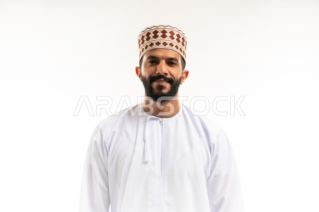التقاط الصور الشخصية للوثائق الرسمية، الاهتمام بالأناقة والمظهر الخارجي، مفهوم الرجولة والثقة بالنفس، بورتريه مقرب لشاب عربي خليجي عماني مبتسم يرتدي الدشداشة و الكمه ينظر الى الكاميرا بإيماءات السرور والسعادة، خلفية بيضاء