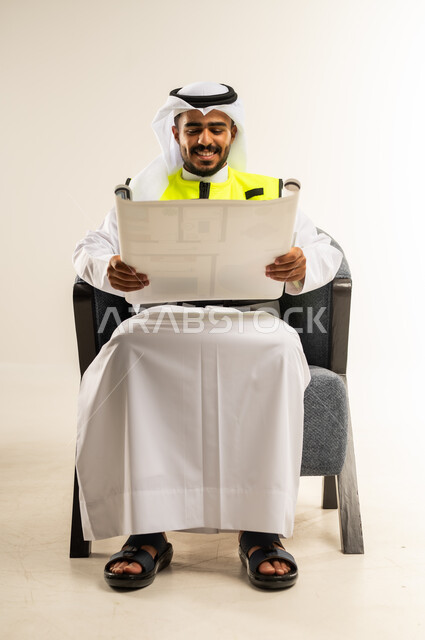 Gestures of joy and happiness, checking and supervising project plans, engineering professions and jobs in Kuwait, portrait of a Kuwaiti Gulf Arab engineer wearing a work gown and protective jacket sitting on a comfortable chair holding an engineering plan in his hand, background White