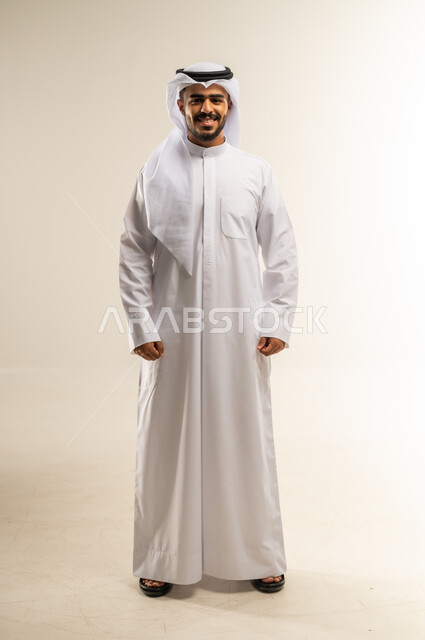 مفهوم الرجولة والثقة بالنفس، الاهتمام بالمظهر الخارجي والأناقة، بورتريه لرجل عربي خليجي كويتي يرتدي الثوب التقليدي والغتره ينظر الى الكاميرا بتعابير السرور، الوقوف باستقامة وثبات، صورة الجسم بالطول الكامل، خلفية بيضاء
