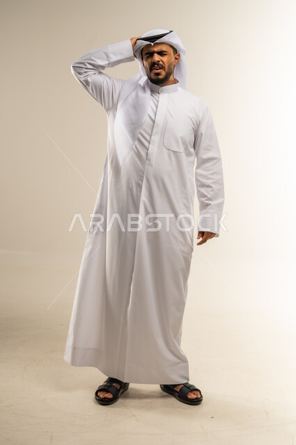 الحاجة للهدوء والراحة، الإحساس بألم الرأس والصداع، المعاناة من آلام الشقيقة، بورتريه لرجل عربي خليجي كويتي يرتدي الثوب التقليدي يضع يده على رأسه بإيماءات التعب و الارهاق, صورة الجسم بالطول الكامل، خلفية بيضاء