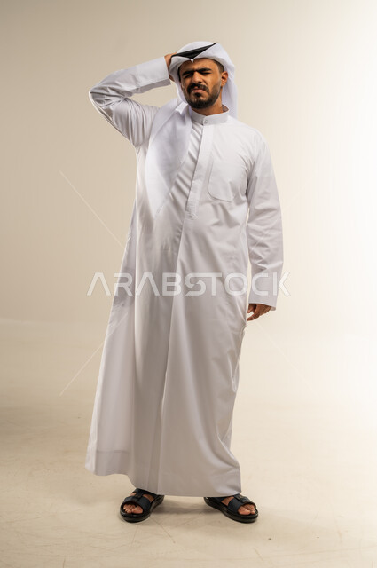 المعاناة من آلام الشقيقة، الحاجة للهدوء والراحة، الإحساس بألم الرأس والصداع، بورتريه لرجل عربي خليجي كويتي يرتدي الثوب التقليدي يضع يده على رأسه بإيماءات التعب و الارهاق, صورة الجسم بالطول الكامل، خلفية بيضاء