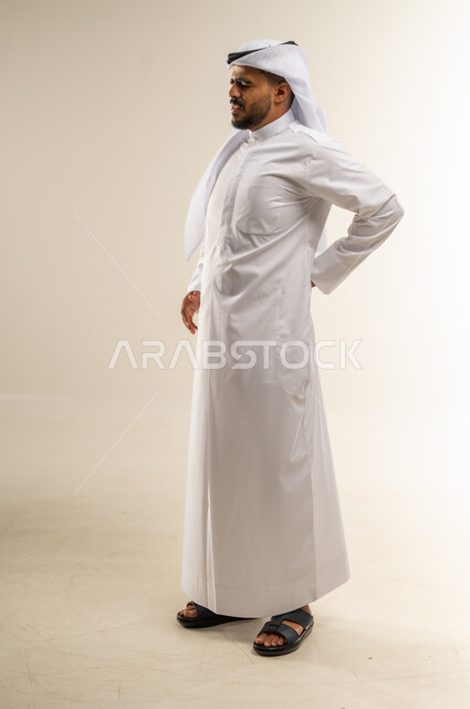التعب والإرهاق و الحاجه للعلاج, أمراض المفاصل و العضلات, الاحساس بألم في العمود الفقري, بورتريه لرجل عربي خليجي كويتي يرتدي الثوب التقليدي يشعر بأوجاع في أسفل الظهر, صورة الجسم بالطول الكامل، خلفية بيضاء