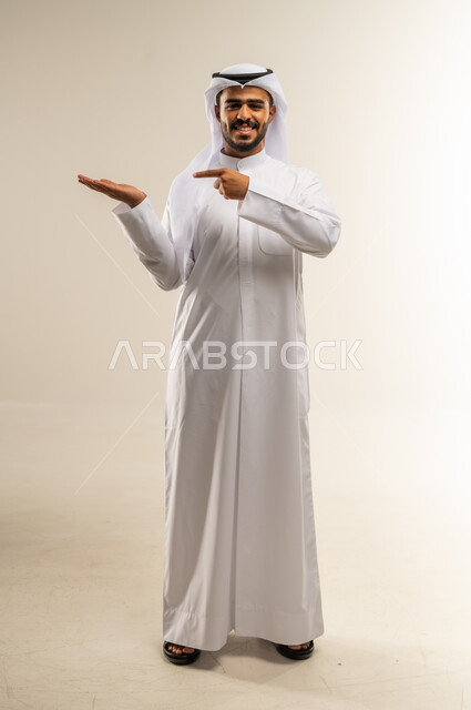 حركة أصابع وإشارات، إيماءات حمل ورفع شيء ما، الإشارة نحو هدف ما، بورتريه لرجل عربي خليجي كويتي يرتدي الثوب التقليدي يشير باصبع السبابة ليده, صورة الجسم بالطول الكامل، خلفية بيضاء