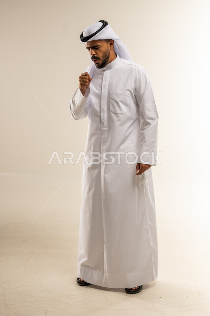 الاحساس بألم البلعوم, مفهوم الاهتمام بالصحة, الاصابة بنزلة برد والتهاب الحلق, بورتريه لرجل عربي خليجي كويتي يرتدي الثوب التقليدي ويقوم بالسعال, صورة الجسم بالطول الكامل، خلفية بيضاء