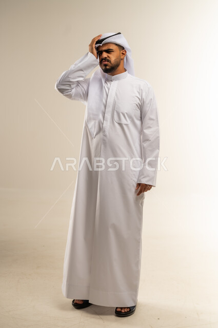 المعاناة من آلام الشقيقة، الحاجة للهدوء والراحة، الإحساس بألم الرأس والصداع، بورتريه لرجل عربي خليجي كويتي يرتدي الثوب التقليدي يضع يده على رأسه بإيماءات التعب و الارهاق, صورة الجسم بالطول الكامل، خلفية بيضاء