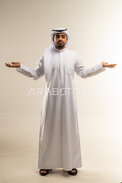 Questioning, interrogation, inquiry about something, expressions of ignorance, surprise and astonishment, portrait of a Kuwaiti Gulf Arab man wearing traditional thobe raising his hands up with gestures of explanation and clarification, full body image, white background