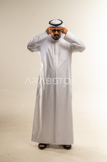 المعاناة من آلام الشقيقة، الحاجة للهدوء والراحة، الإحساس بألم الرأس والصداع، بورتريه لرجل عربي خليجي كويتي يرتدي الثوب التقليدي يضع يده على رأسه بإيماءات التعب و الارهاق, صورة الجسم بالطول الكامل، خلفية بيضاء