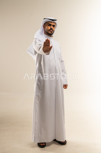 طلب التوقف عن فعل شيء ما، فتح الكف ورفعها في الهواء بتعابير الحزم والنهي، بورتريه لرجل عربي خليجي كويتي يرتدي الثوب التقليدي يرفع يده بإيماءات الغضب، الجسم بالطول الكامل، خلفية بيضاء
