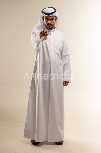 الإشارة باصبع السبابة إلى الكاميرا بشكل مباشر، التهديد والتوعد بتنفيذ شيء ما، إيماءات الترهيب والتحذير، توجيه أصابع الاتهام إلى شخص معين، بورتريه لرجل عربي خليجي كويتي يرتدي الثوب التقليدي والغتره يشير إلى مكان ما محدد، الجسم بالطول الكامل، خلفية بيضاء