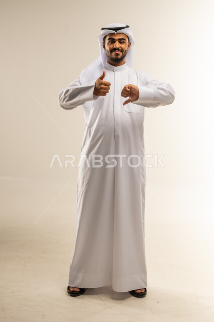 الحيادية في موضوع ما وعدم الانحياز لجهة معينة، بورتريه لشاب عربي خليجي كويتي يرتدي الثوب التقليدي يشير باصابع يده إلى الأعلى والأسفل بشكل متعاكس، حركات وجه ويدين مختلفة، إيماءات الجمود والبرود في اتخاذ القرار، الجسم بالطول الكامل، خلفية بيضاء