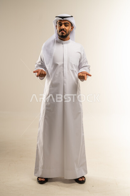 التردد وعدم الثقة بخصوص أمر معين، بورتريه  لرجل عربي خليجي كويتي يرتدي الثوب التقليدي يرفع كفيه للاعلى بإيماءات عدم التأكد، الشعور بالحيرة وعدم المعرفة، صورة الجسم بالطول الكامل، خلفية بيضاء