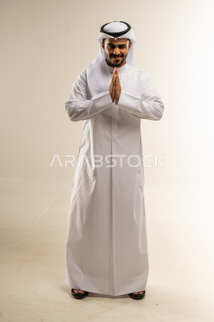 مفهوم الشكر والامتنان، إيماءات الطلب والتوسل، بورتريه لرجل عربي خليجي كويتي يرتدي الثوب التقليدي والغترة يرفع يديه باستعطاف، الرغبة في تحقيق الأمنيات، الجسم بالطول الكامل، خلفية بيضاء