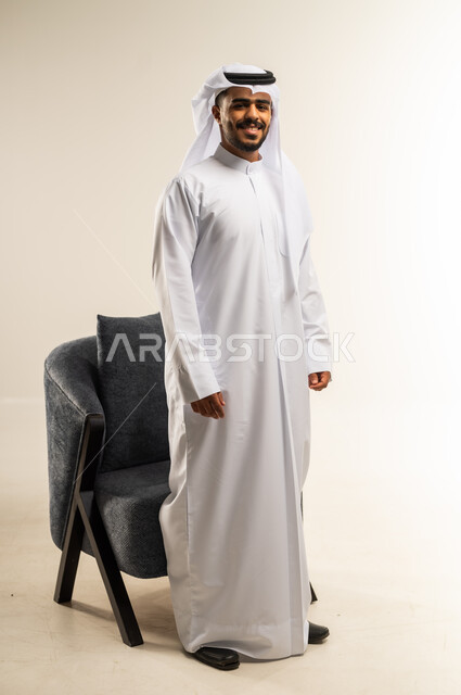 مفهوم الرجولة والثقة بالنفس، الاهتمام بالمظهر الخارجي والأناقة، بورتريه لرجل عربي خليجي كويتي يرتدي الثوب التقليدي ينظر الى الكاميرا بتعابير السرور، الوقوف باستقامة وثبات، صورة الجسم بالطول الكامل، خلفية بيضاء