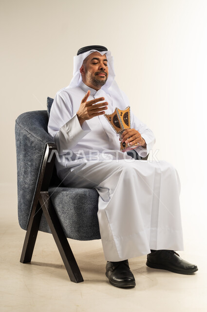 العادات والتقاليد العريقة في الكويت, بورتريه لسيد عربي خليجي كويتي يرتدي الثوب التقليدي يجلس على كرسي مريح يقوم بالتطيب و التعطر من البخور( المبخرة )الاهتمام بالمظهر الخارجي، استخدام خشب العود في الأعياد والمناسبات، , خلفية بيضاء