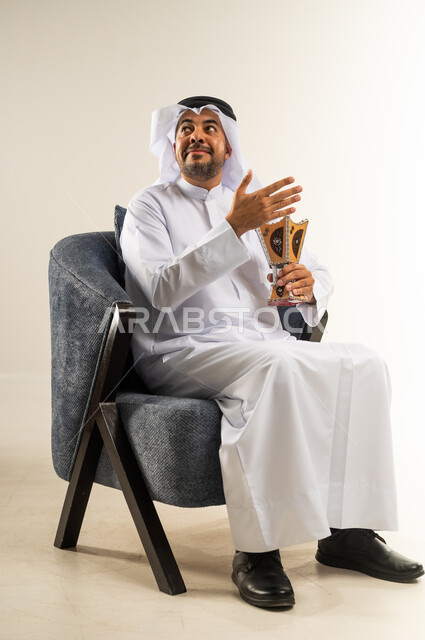 استخدام خشب العود في الأعياد والمناسبات، بورتريه لسيد عربي خليجي كويتي يرتدي الثوب التقليدي يجلس على كرسي مريح يقوم بالتطيب و التعطر من البخور( المبخرة ) ينظر إلى شيء ما في الأعلى, العادات و التقاليد العريقة في الكويت, خلفية بيضاء