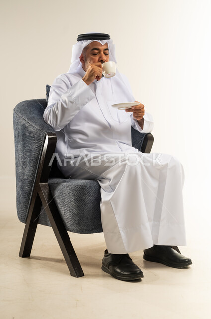 الحيوية والنشاط عند شرب الكافيين، الاستمتاع والاحساس بالدفء عند تناول المشروبات الساخنة، بورتريه لرجل عربي خليجي كويتي يرتدي الثوب التقليدي والغترة يحمل بيده كوب القهوة، خلفية بيضاء