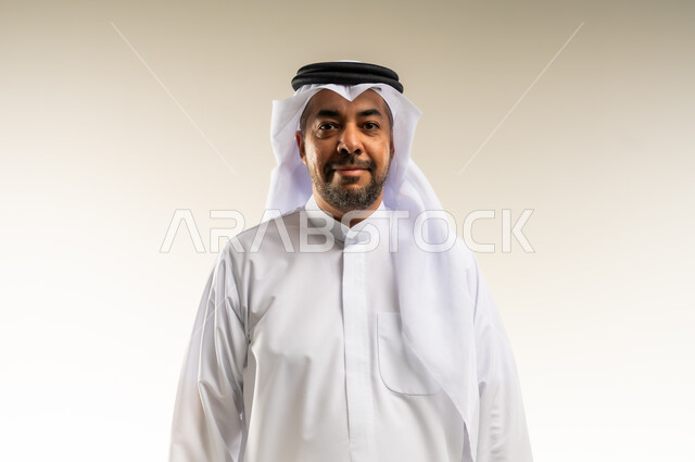 The concept of handsomeness, masculinity and strength, interest in elegance and external appearance, close-up portrait of a smiling Kuwaiti Gulf Arab man wearing traditional thobe and ghutra looking at the camera with gestures of pleasure and self-confidence, taking pictures of personal documents, white background