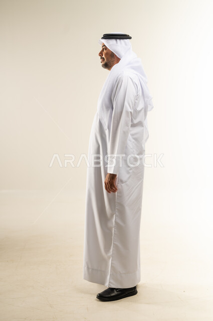 التقاط صور للوثائق الشخصية، مفهوم الوسامة والرجولة والقوة، الاهتمام بالأناقة والمظهر الخارجي، بورتريه من الجانب لرجل عربي خليجي كويتي يرتدي الثوب التقليدي والغترة يقف باستقامة وثقة في النفس، الجسم الكامل بالطول، خلفية بيضاء