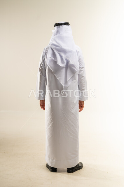 الاهتمام بالأناقة والمظهر الخارجي، مفهوم الوسامة والرجولة والقوة، بورتريه من الخلف لرجل عربي خليجي كويتي يرتدي الثوب التقليدي والغترة يقوم بمحادثة ومخاطبة شخص ما، الجسم الكامل بالطول، خلفية بيضاء