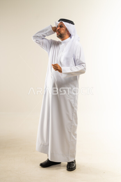 الاحساس بالشقيقية والصداع النصفي, الشعور بالإرهاق وفقدان التركيز, الاجهاد والضغط النفسي, بورتريه لرجل عربي خليجي كويتي يرتدي الثوب والغترة يضع يديه على رأسه ويغمض عينيه بإيماءات ألم الرأس الشديد, صورة الجسم بالطول الكامل, خلفية بيضاء