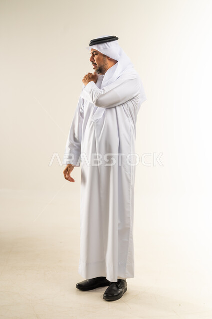 الأوجاع والآلام العصبية والعضلية، طلب المساعده والحاجه للعلاج، التهاب العضلات والمفاصل، بورتريه من الجانب لرجل عربي خليجي كويتي يرتدي الثوب التقليدي والغترة يضع يده على كتفه بايماءات الألم والتعب والأرهاق، صورة الجسم الطول الكامل, خلفية بيضاء