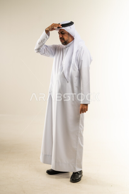 الاحساس بالشقيقية والصداع النصفي, الشعور بالإرهاق وفقدان التركيز, الاجهاد والضغط النفسي, بورتريه لرجل عربي خليجي كويتي يرتدي الثوب والغترة يضع يديه على رأسه ويغمض عينيه بإيماءات ألم الرأس الشديد, صورة الجسم بالطول الكامل, خلفية بيضاء